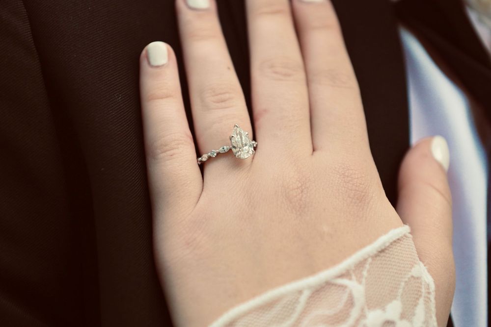 Close-up of a diamond engagement ring on a woman's finger, featuring elegant side stones in a silver setting.