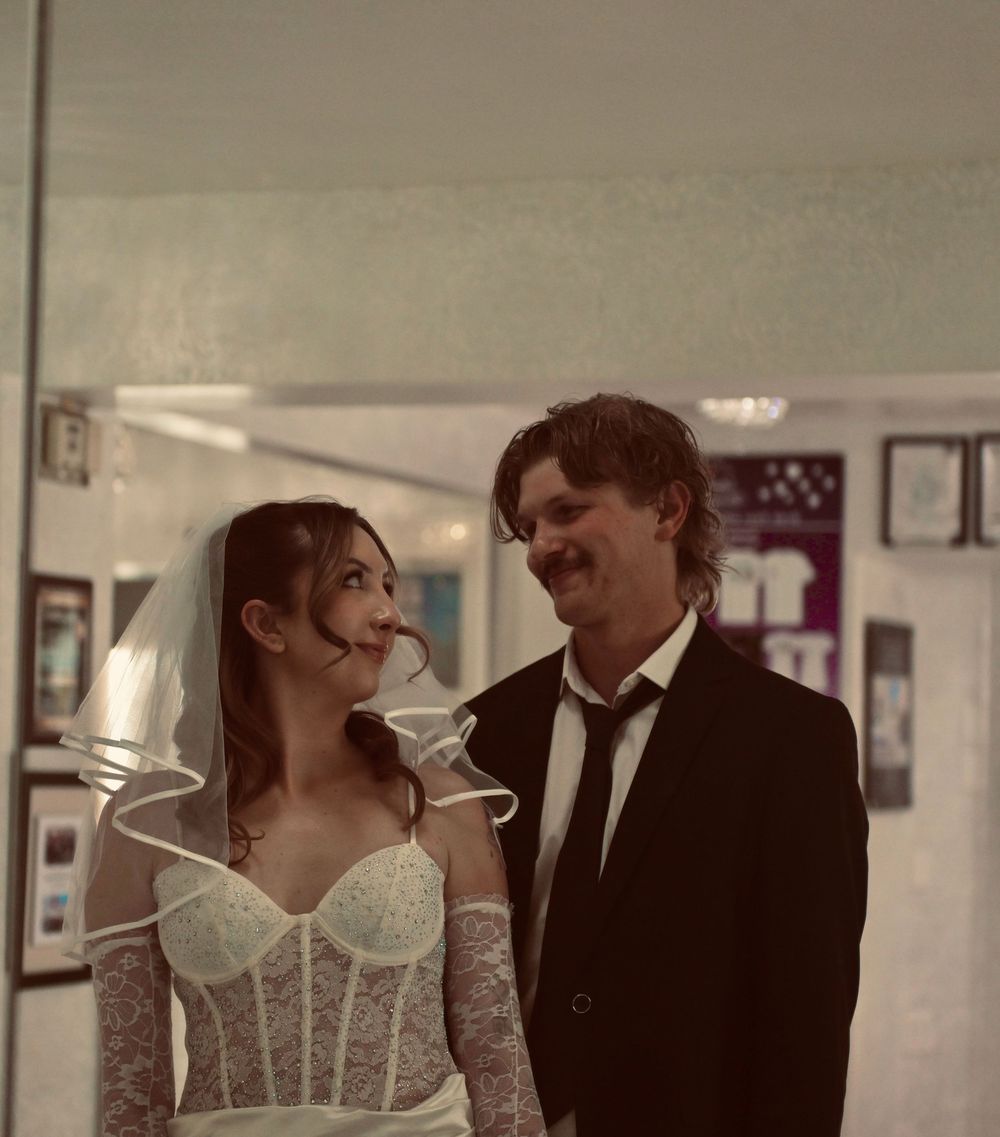 Bride in lace corset gown and veil smiles at groom in black suit inside a Las Vegas wedding chapel.