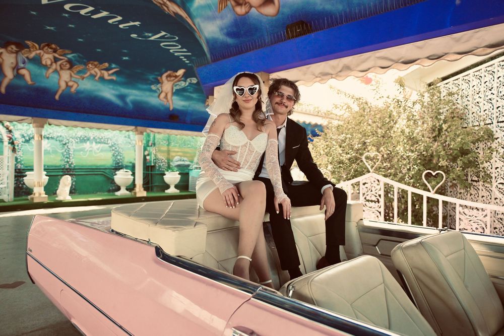 Couple posing in a pink vintage convertible car at a romantic fairground attraction.