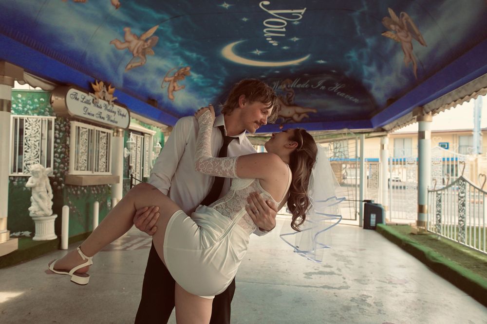 Romantic couple sharing a dip kiss in a decorated venue with fairy mural ceiling during a formal event.