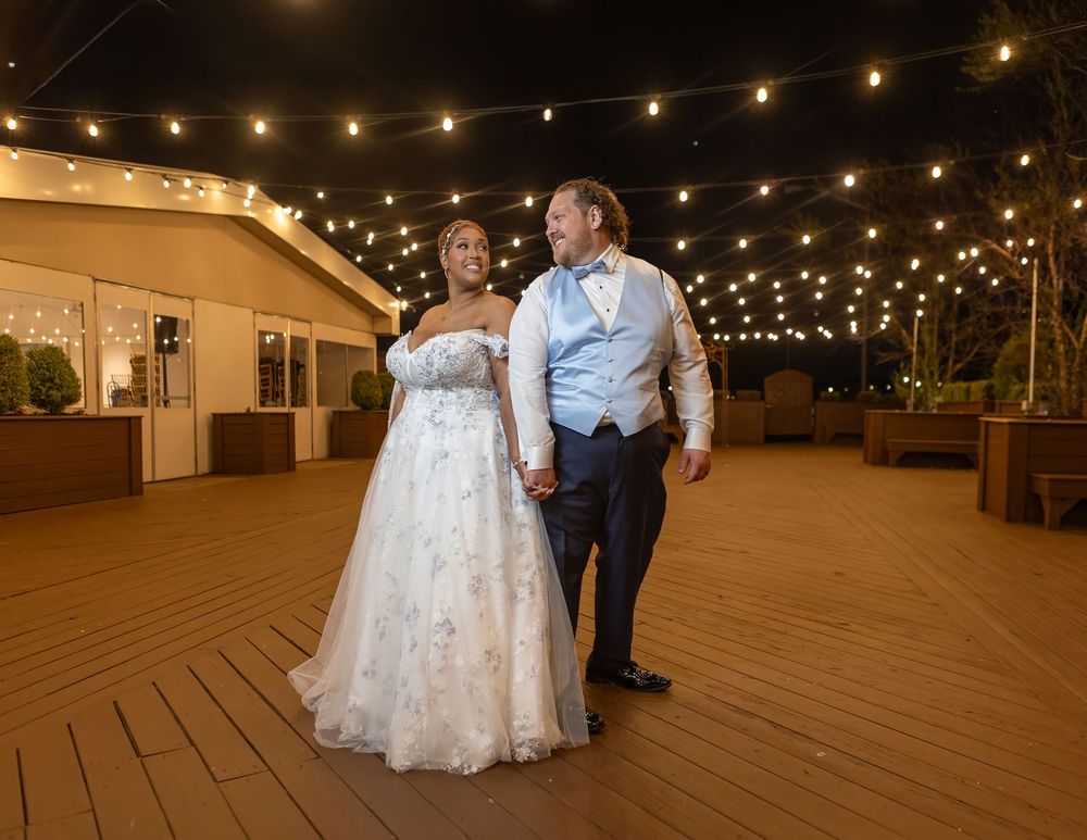 Bride and groom share romantic first dance on decorated outdoor deck with string lights at night.