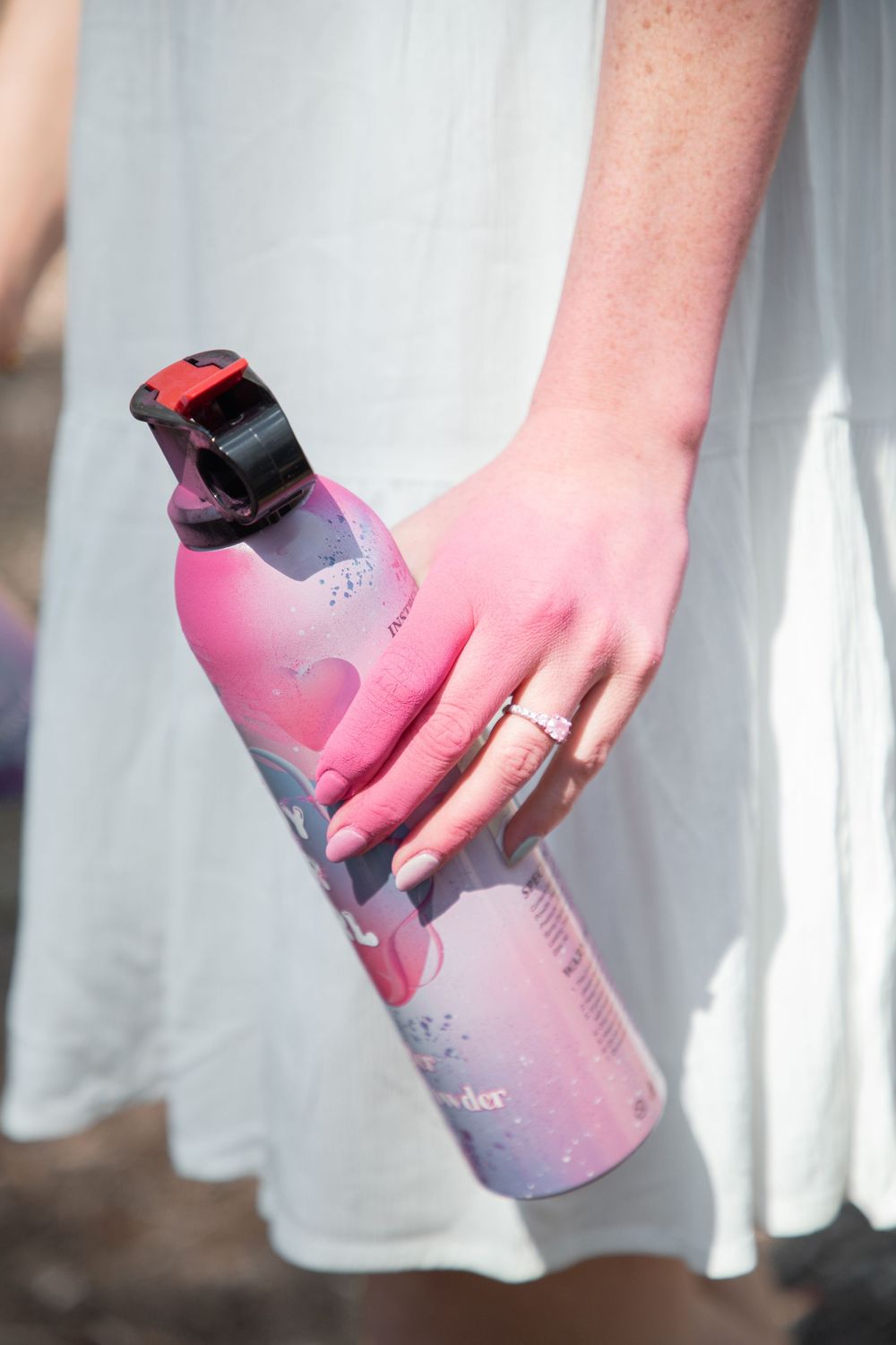 Woman in white dress holding a pink floral water bottle with a black lid outdoors.