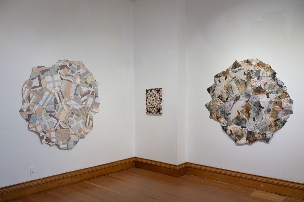 Three mixed-media wall sculptures in neutral tones displayed in a white gallery corner with hardwood floors.