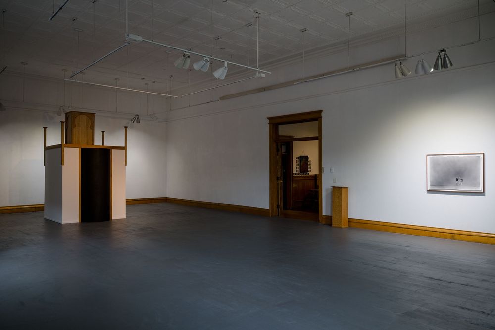 Modern art gallery interior with wooden installations, track lighting, and a framed artwork on white wall.