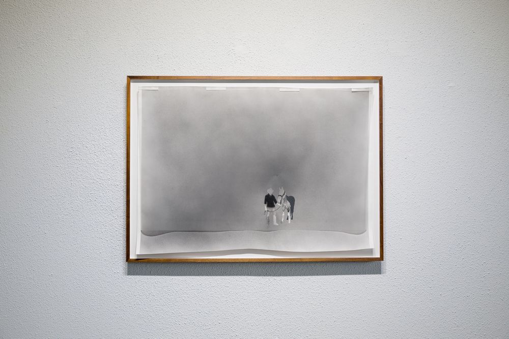 Framed artwork of a small cow standing alone in a misty gray landscape, displayed on a white gallery wall.
