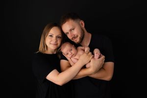 Family portrait against black background in matching dark outfits with loving embrace.