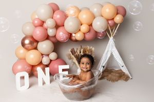 Pink, peach, and white balloon garland arranged in an elegant arch with a birthday party setup on a gray background.