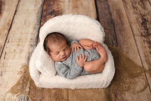 Peaceful newborn sleeping in white cushioned basket on wooden background.
