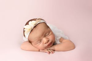 Sleeping newborn wearing cream bow headband rests peacefully on pink background.Newborn photography in Milton Keynes