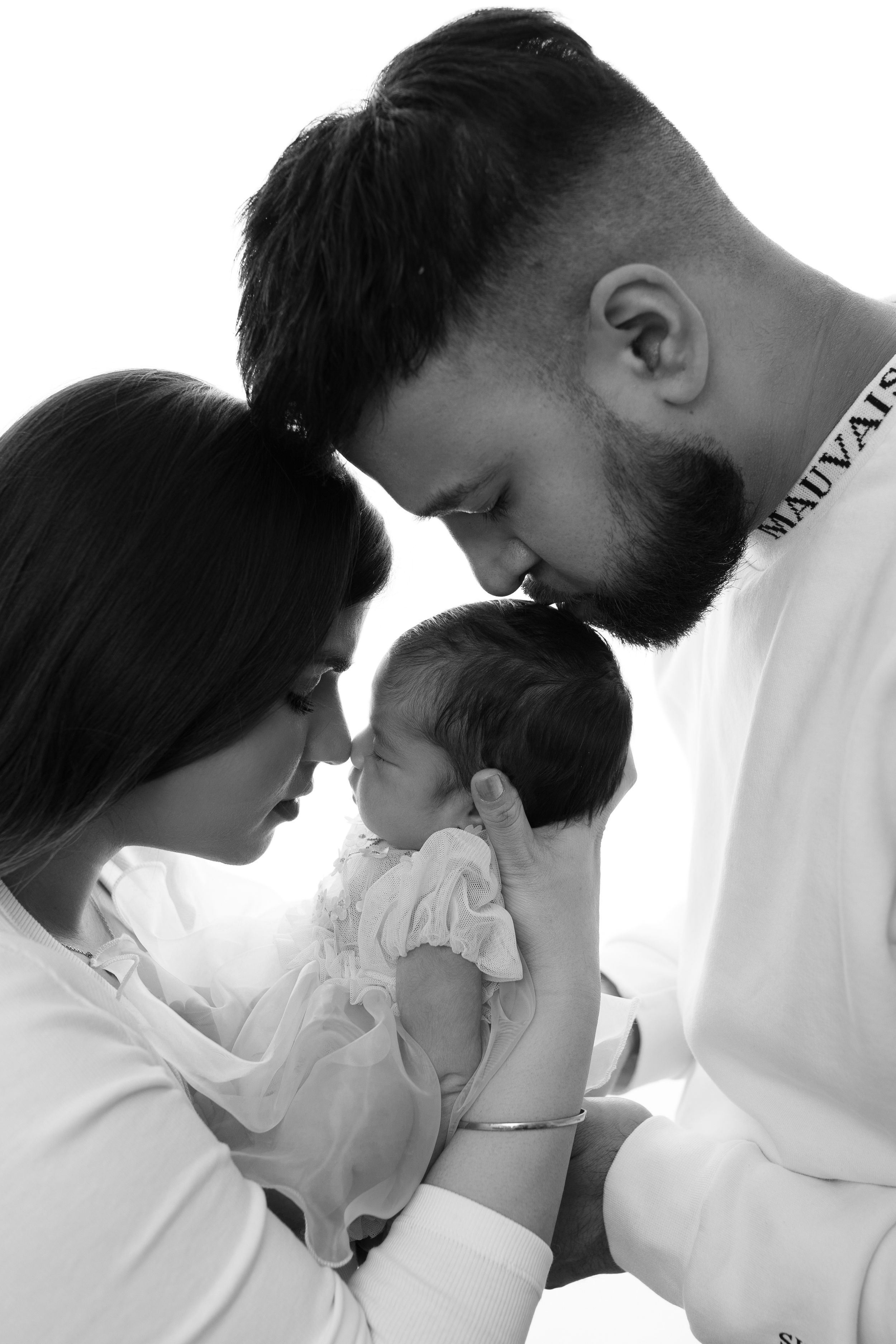 A tender sequence showing parents leaning close to their newborn baby in gentle black and white moments.