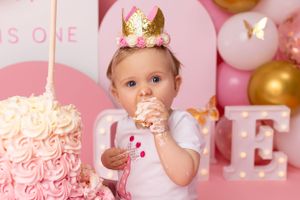 First birthday celebration with pink cake, crown, and balloon decorations.