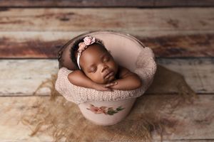 Sleeping baby cozily nestled in a pink bowl with soft fabric on rustic wooden background.