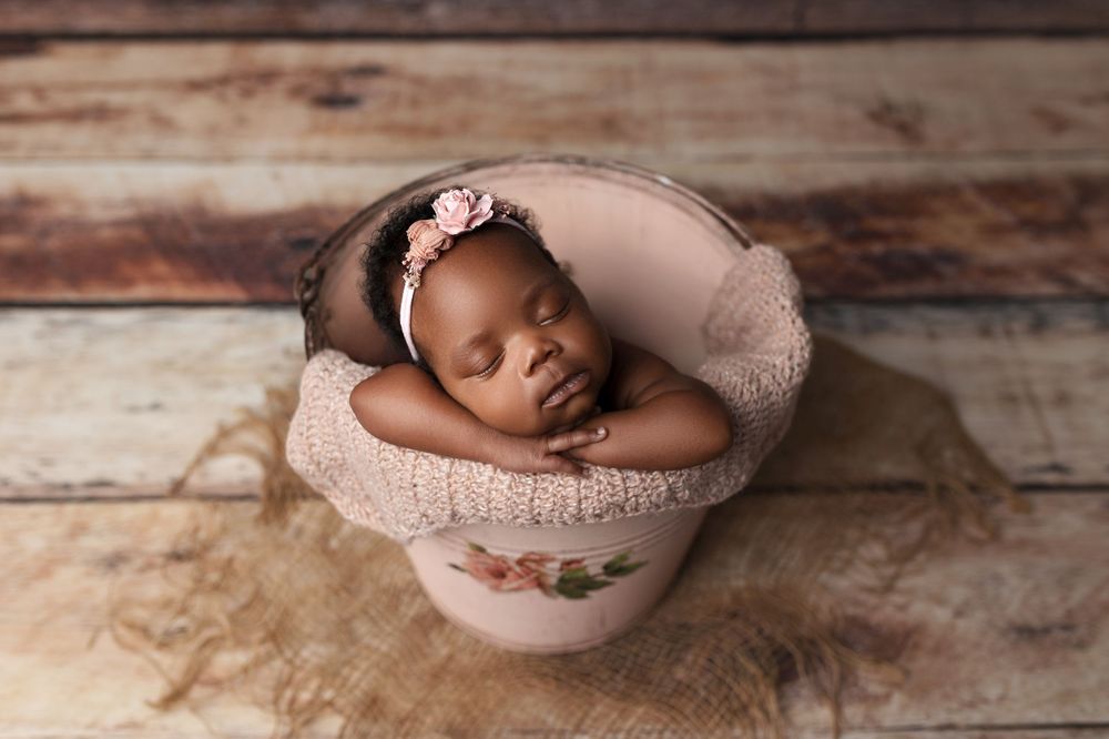 Sleeping baby cozily nestled in a pink bowl with soft fabric on rustic wooden background.