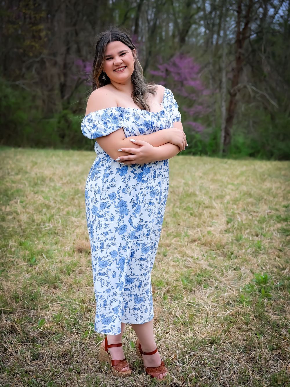 Outdoor photo series in a blue floral dress against natural grass and wooded backdrop.