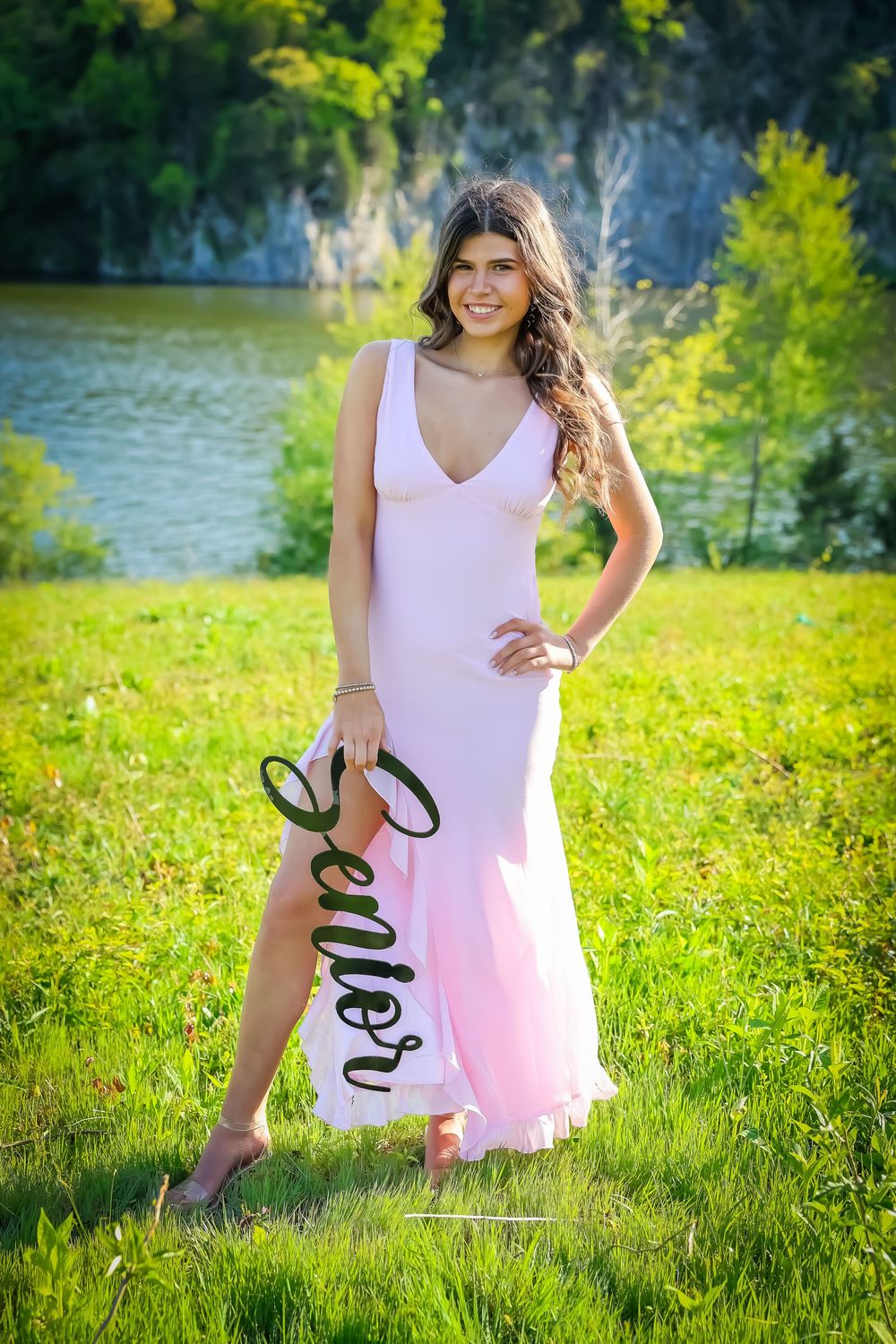 Summer photoshoot in a pink dress against scenic lake and cliff backdrop.