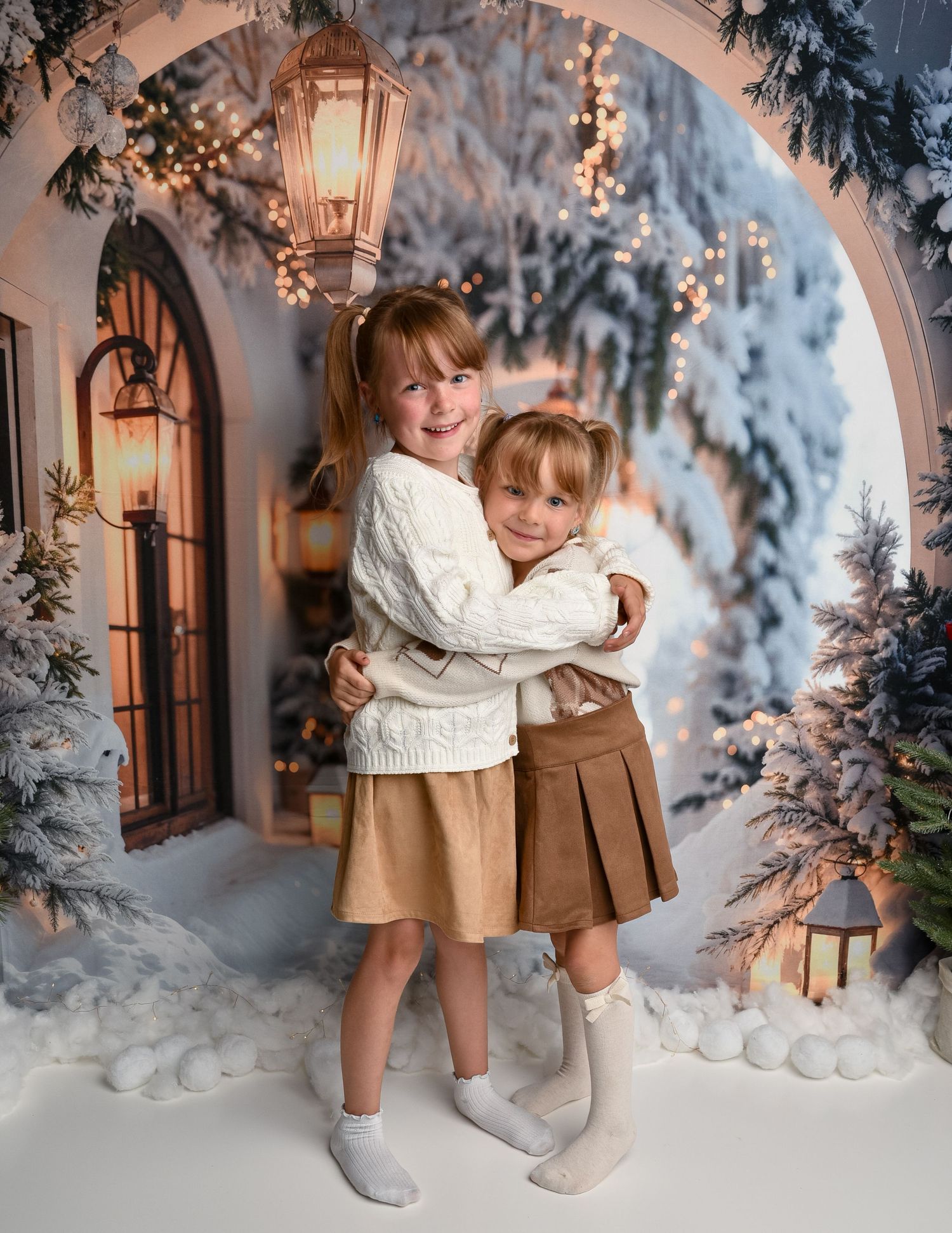 Christmas Mini Wolverhampton — Two girls hugging beneath a hanging lantern in a snowy Christmas street backdrop.