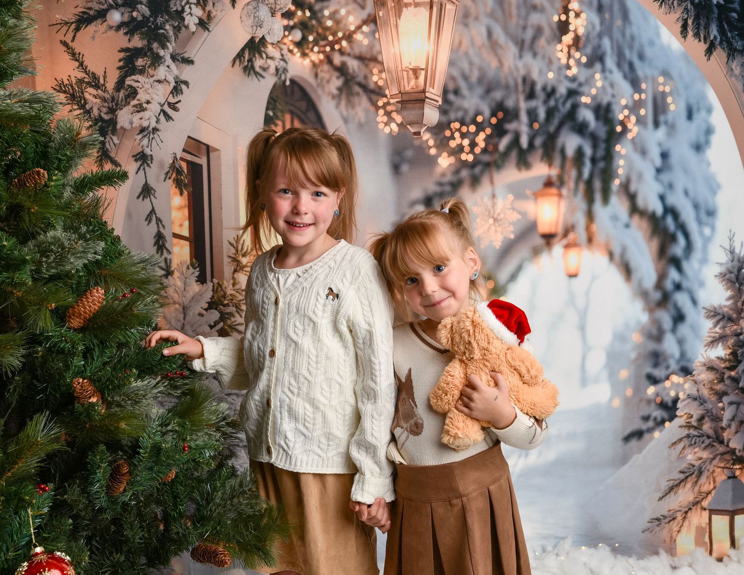 Christmas Mini Wolverhampton — Two girls playing beside a Christmas tree and hugging a teddy bear in a snowy outdoor Christmas scene.