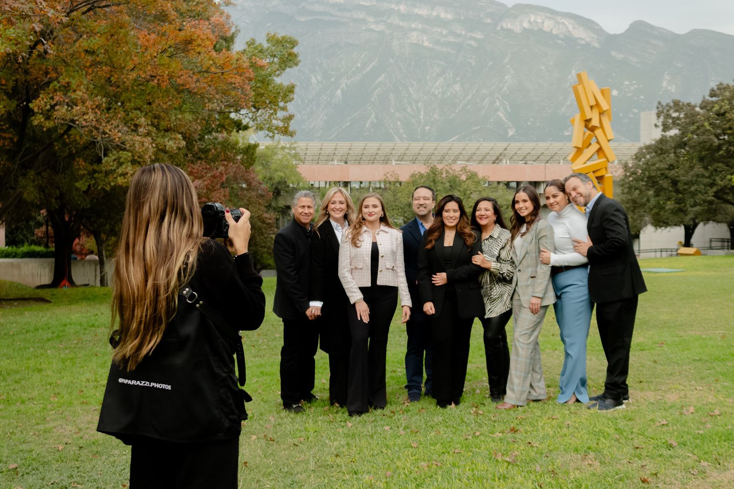 Photographer captures a group of people posing on a green lawn with mountains in the background.
