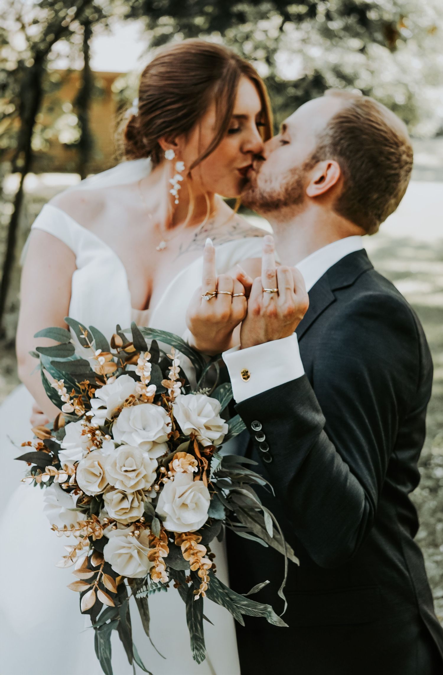 Elegant white and gold wedding bouquet with roses and greenery against blurred background.