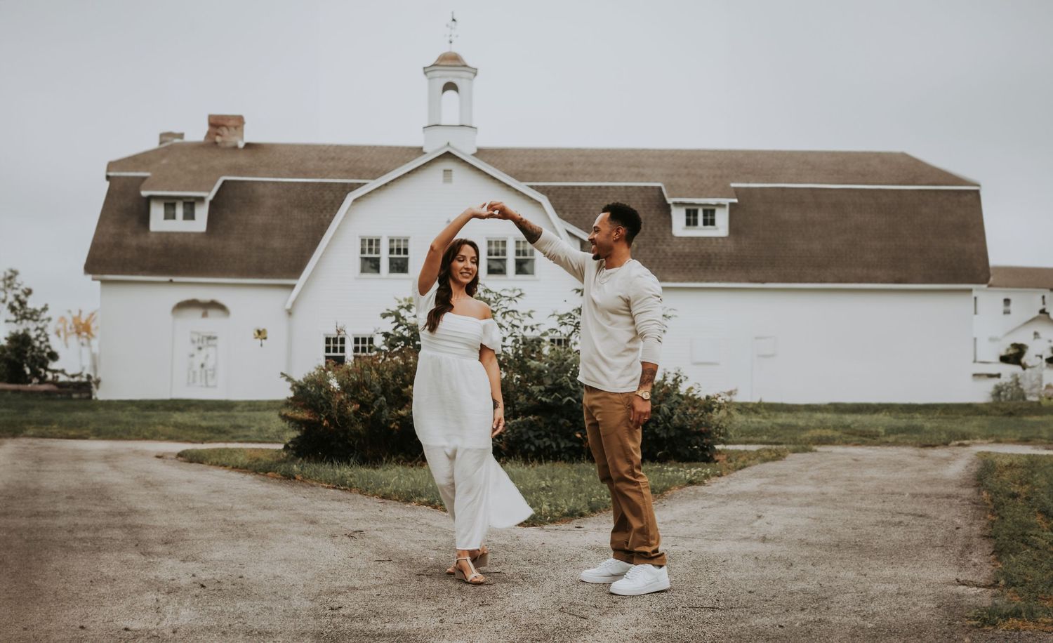 Rustic farmhouse wedding venue with white chapel and brown roof under cloudy sky.