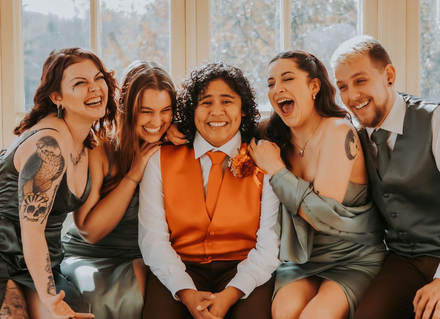 Candid photo of wedding party members laughing together on a couch by a window.