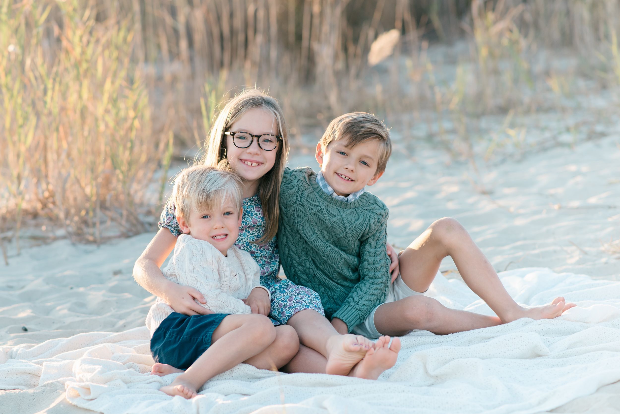 Three siblings snuggle together on a white blanket at Fisherman's Cove in Manasquan, New Jersey.