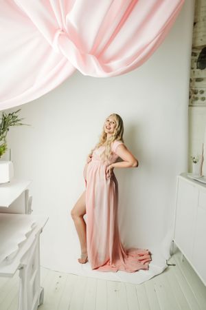 Woman in flowing pink dress twirls and dances in a bright white studio space.