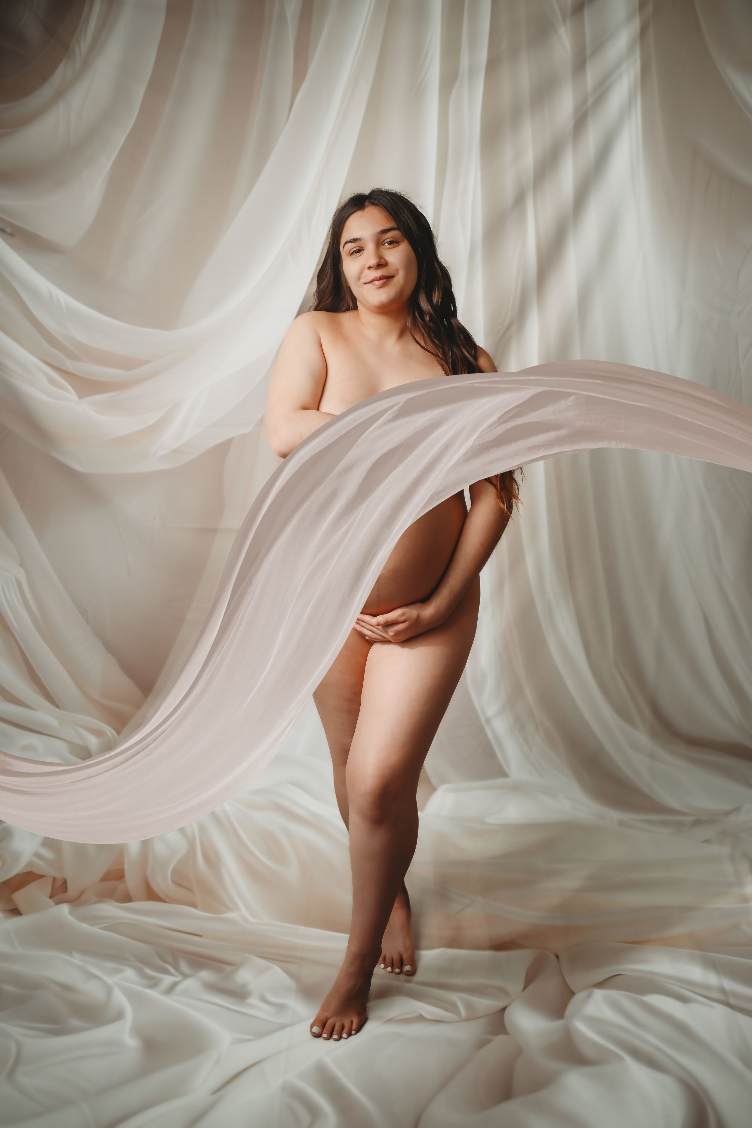 Ethereal maternity portrait with flowing white fabric in studio setting.