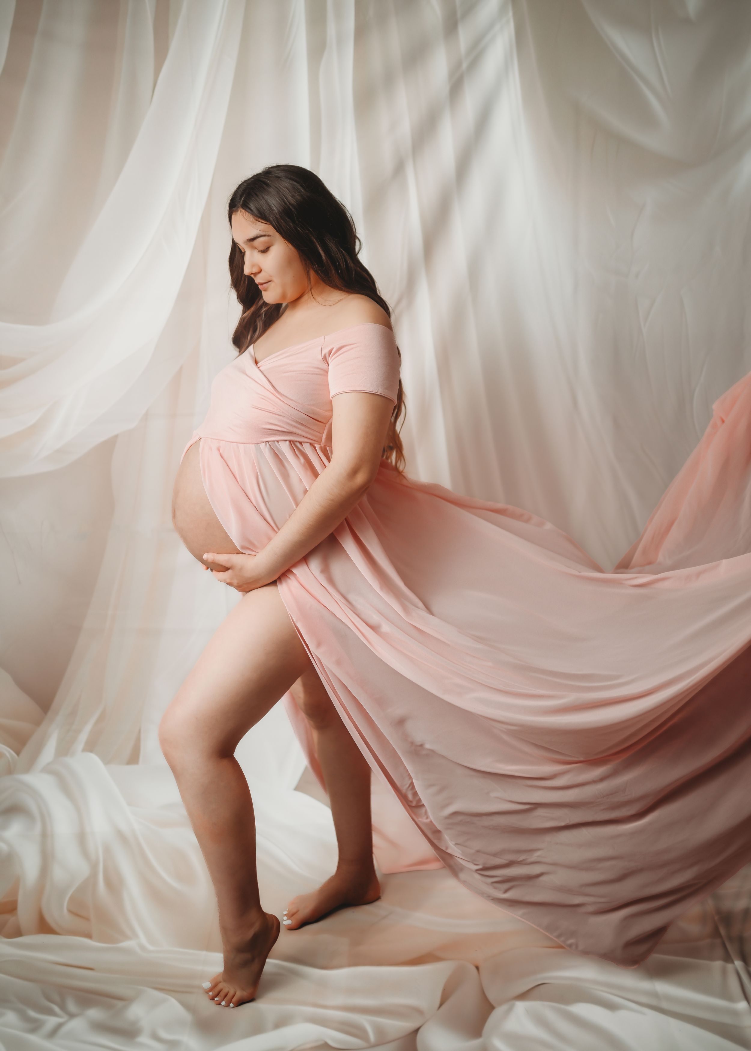 Elegant maternity photo with billowing pink fabric against white backdrop.