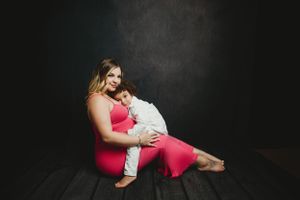 Intimate maternity photography session showing mother-child connection against dark background.