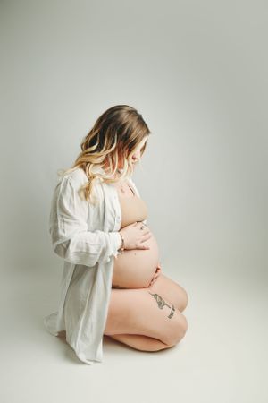 Artistic maternity photo of an expectant mother in a white button-down shirt against a neutral background.