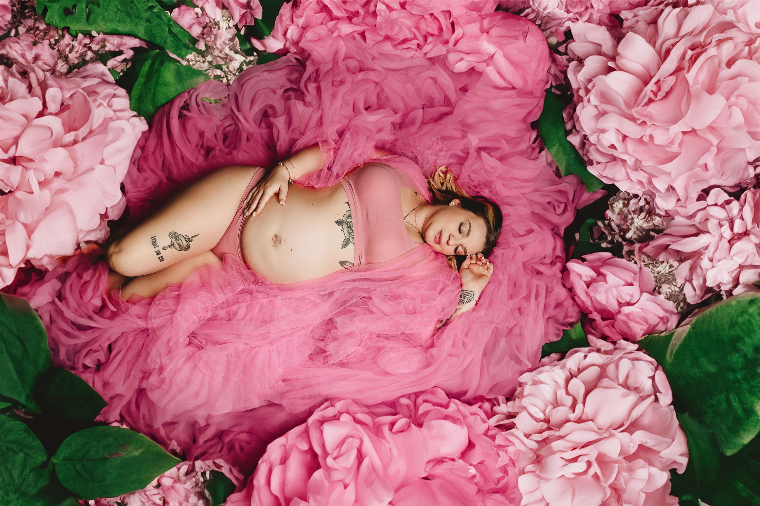 Maternity portrait surrounded by pink peonies and green foliage.
