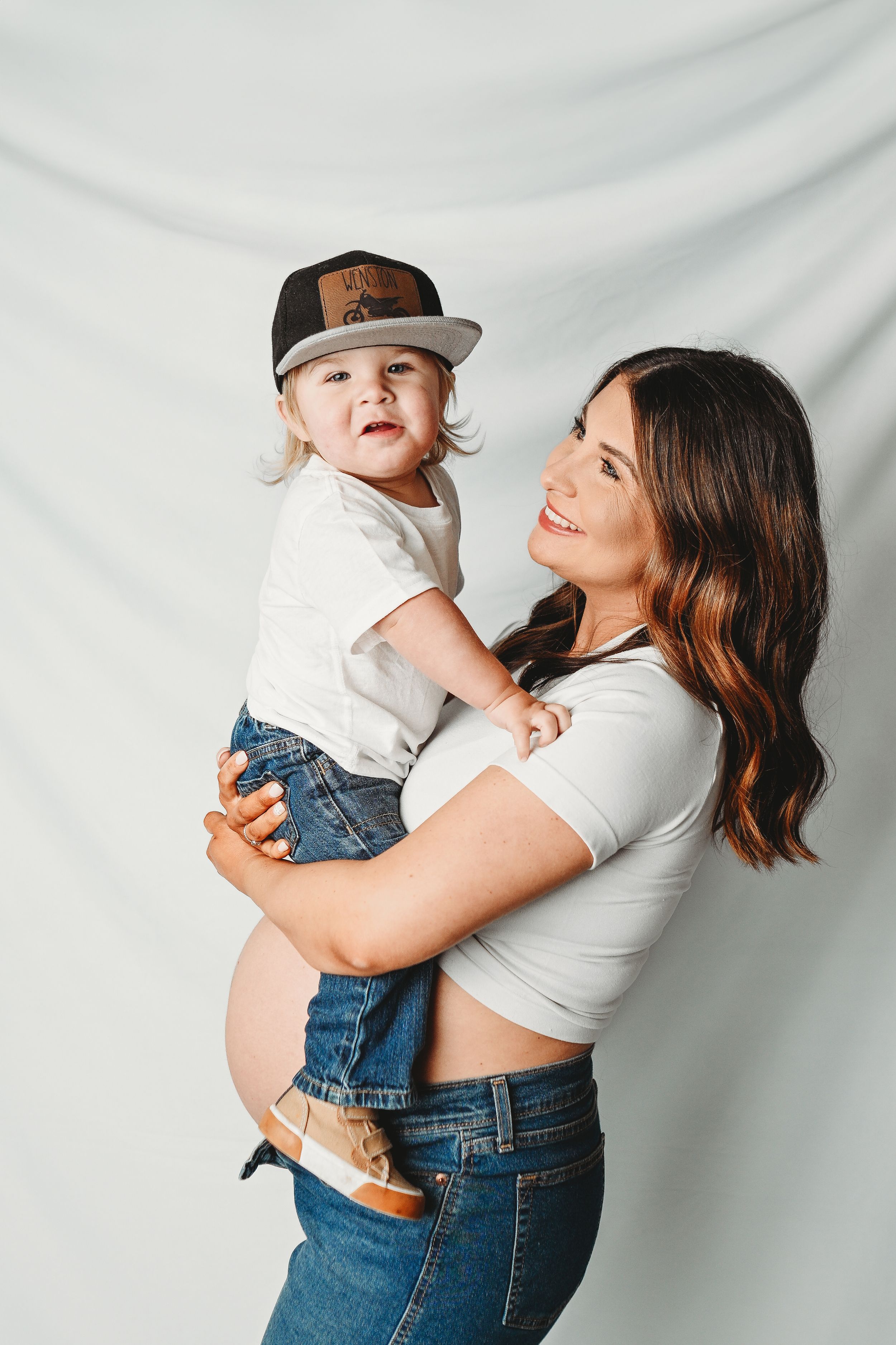 Mother and child in matching denim sharing playful moments against white backdrop.