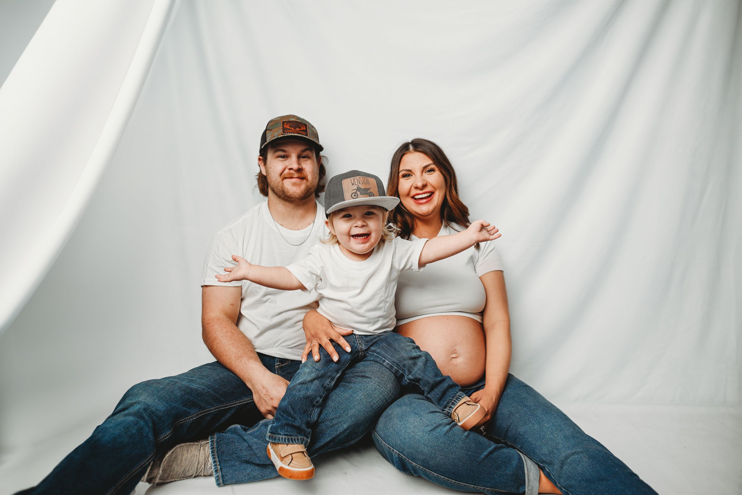 Family photo session with casual denim and white outfits against light backdrop.