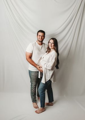 Couple's maternity photoshoot against white backdrop showing playful poses.