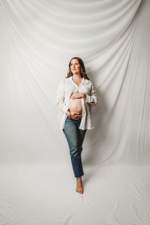 Artistic maternity portraits against white backdrop showcasing pregnancy silhouette.