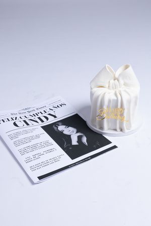 White gift bag with gold Happy Birthday text next to a newspaper on light background.