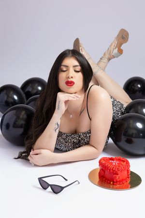 Glamorous portrait with red cake and black balloons in studio setting.