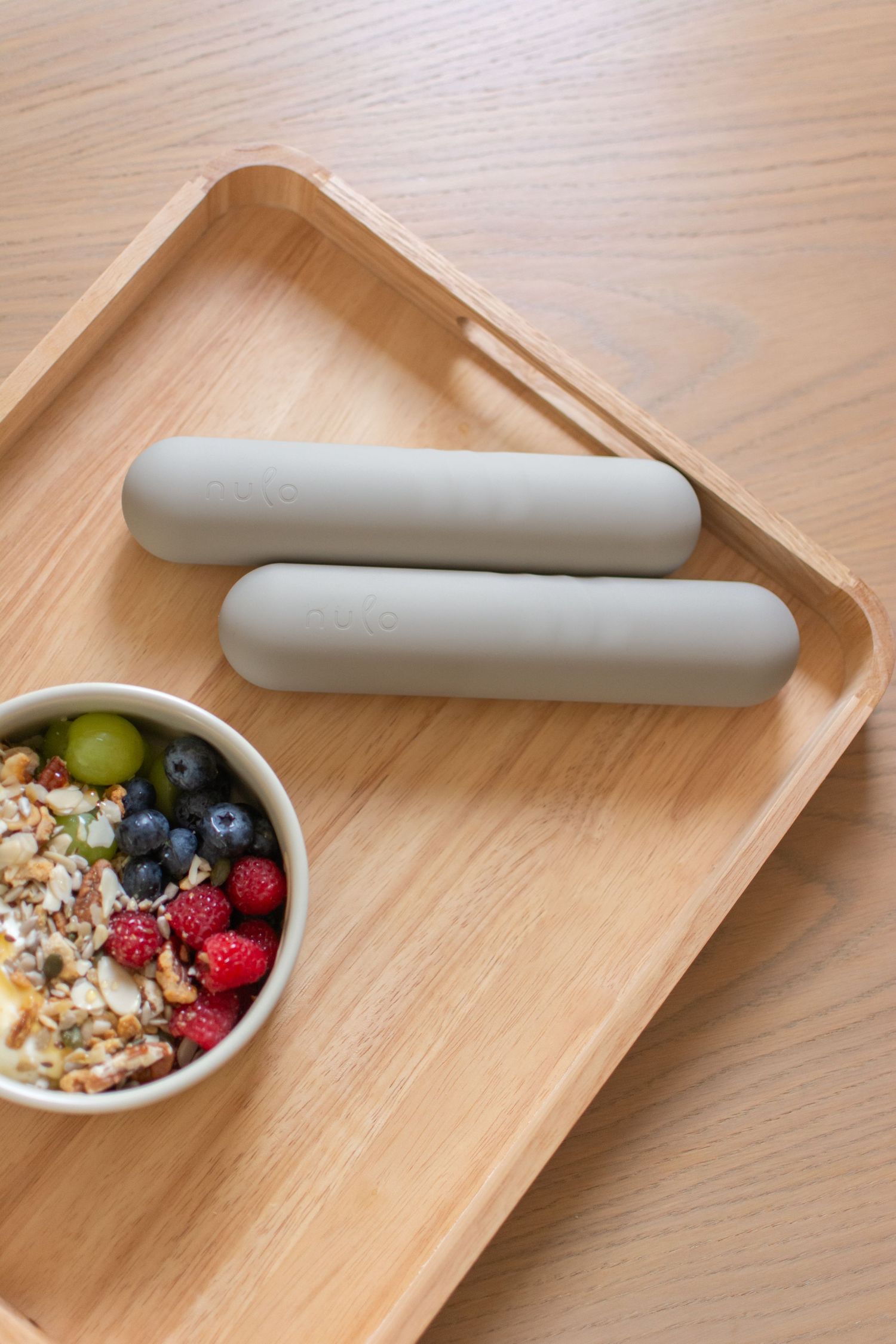 Wooden tray with two nulo hand weights and a bowl of granola topped with fresh berries and grapes.