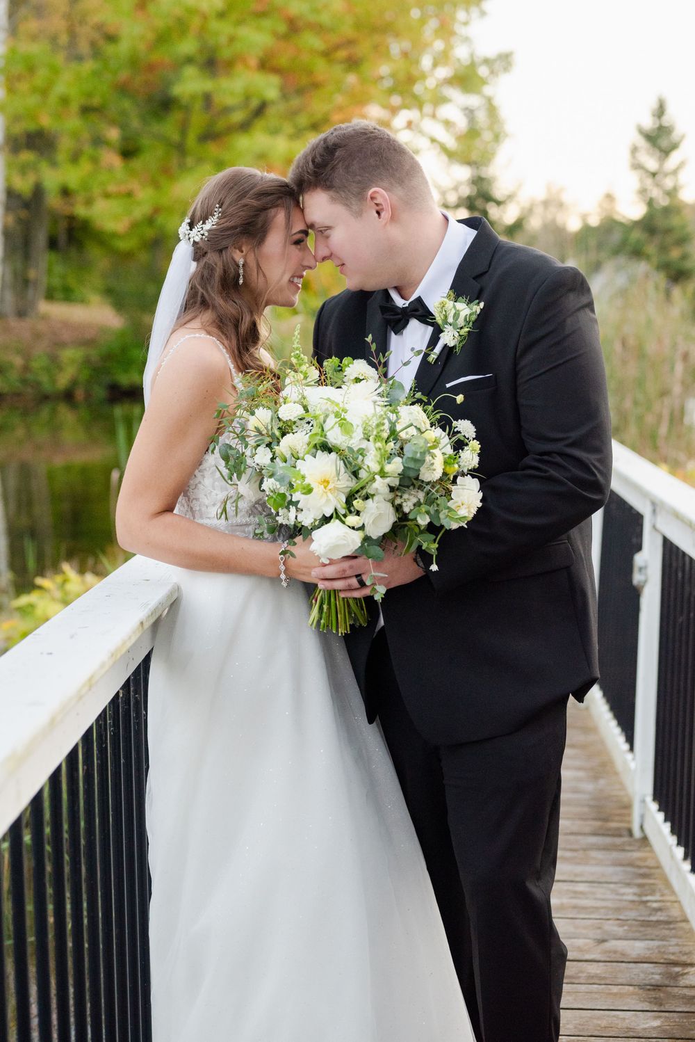 A romantic wedding moment shared on a wooden bridge with a beautiful white floral bouquet in autumn.