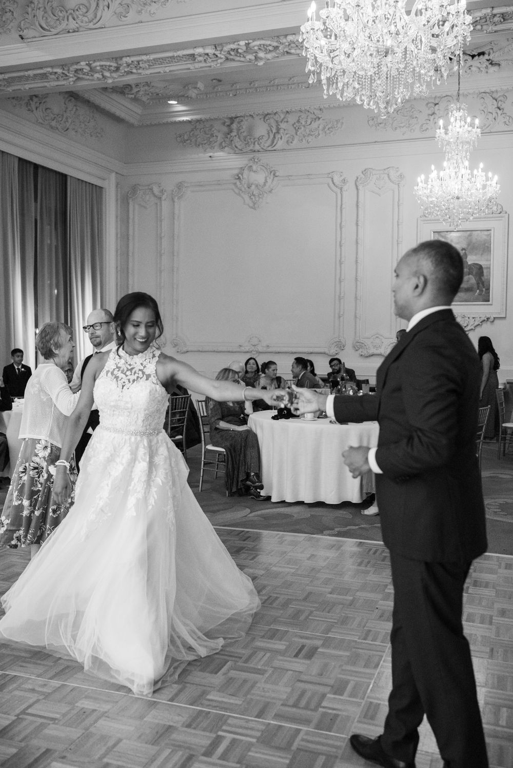A couple shares their first dance at an elegant ballroom wedding reception with crystal chandeliers and ornate decor.