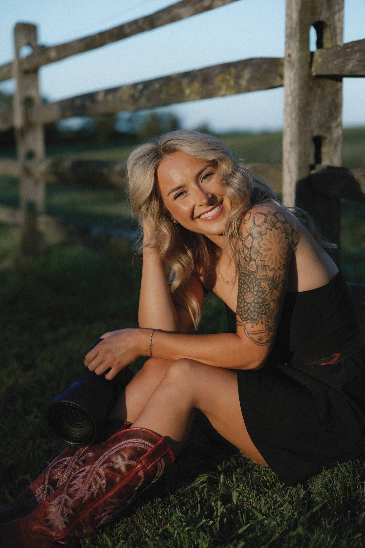 Rustic outdoor portrait session with wooden fence and cowboy boots at sunset.