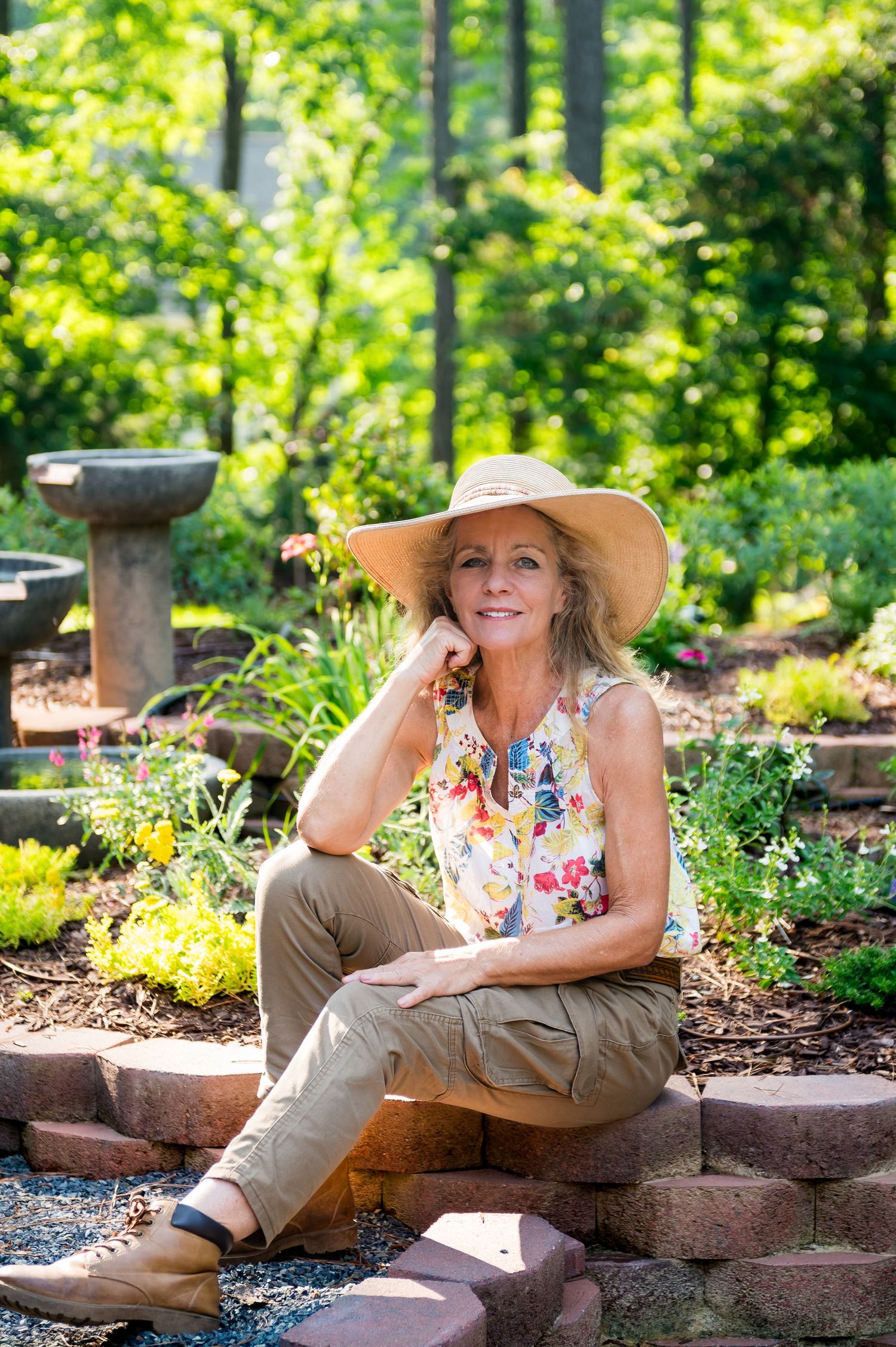 Woman in sun hat and floral dress lying on landscaped garden stones on sunny day.