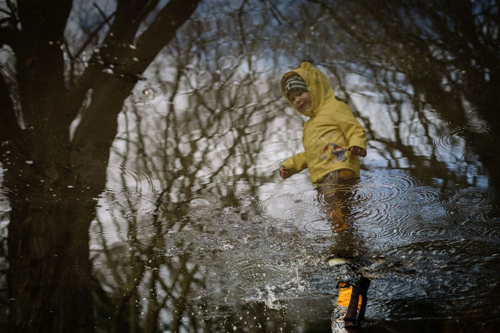 A person in a yellow raincoat splashes energetically through a puddle on a rainy day.