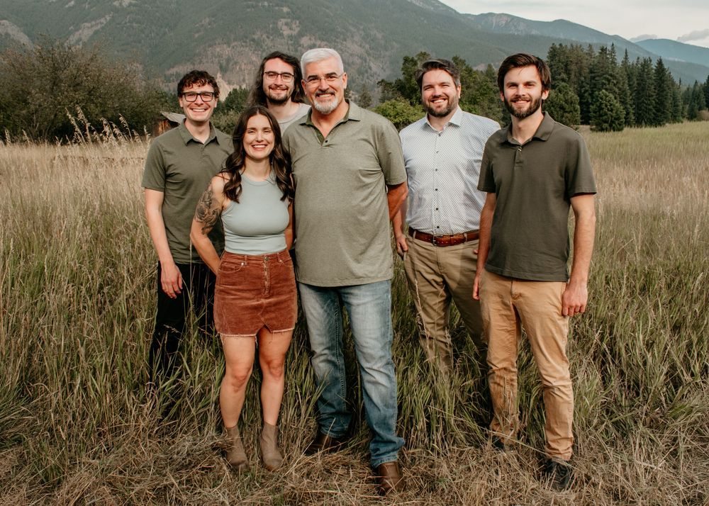 A group of people pose together in an outdoor field with mountains and natural scenery in the background.