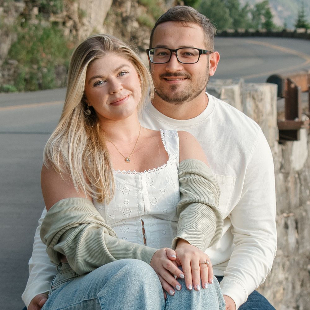 A couple sits close together outdoors sharing an intimate moment while wearing casual white sweaters.