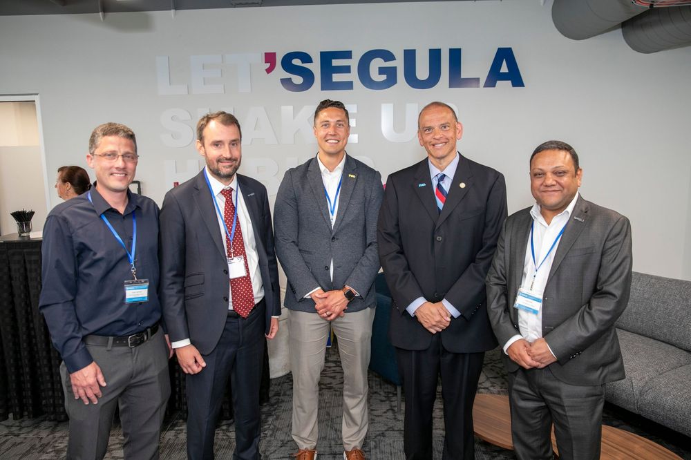 Five professionals posing together at a Segula Technologies corporate event in a modern conference venue.