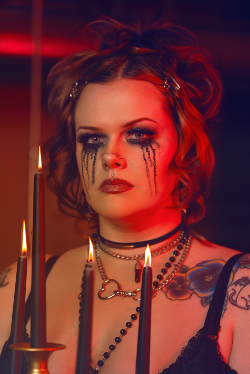 Gothic makeup look with black tears and red lighting creates dramatic portrait with candles.