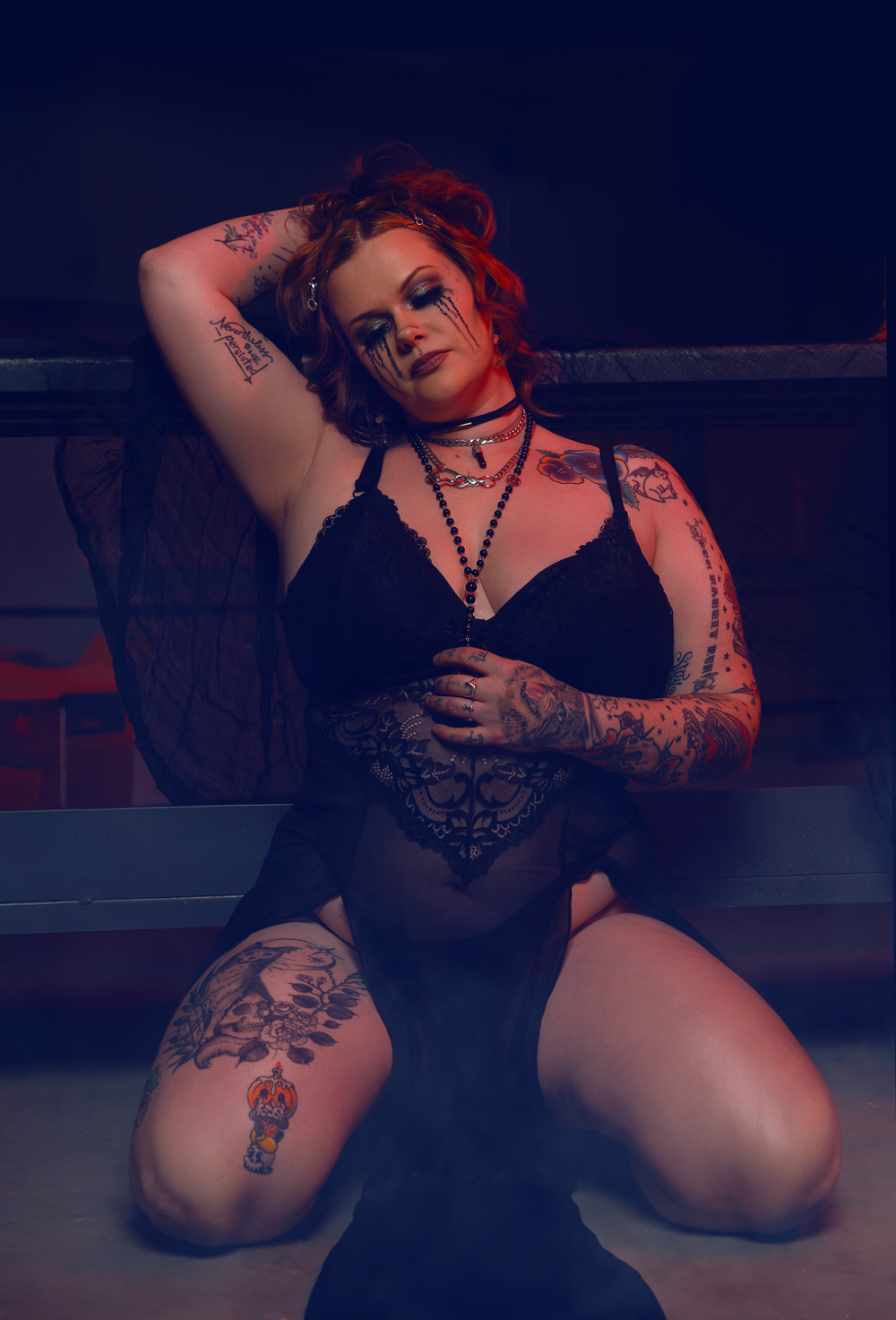 Gothic boudoir photo with dramatic lighting and tattoos in dark setting.