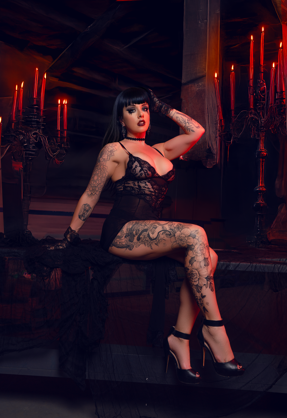 Gothic model in lace lingerie poses with tattoos on dark stage with red candles.